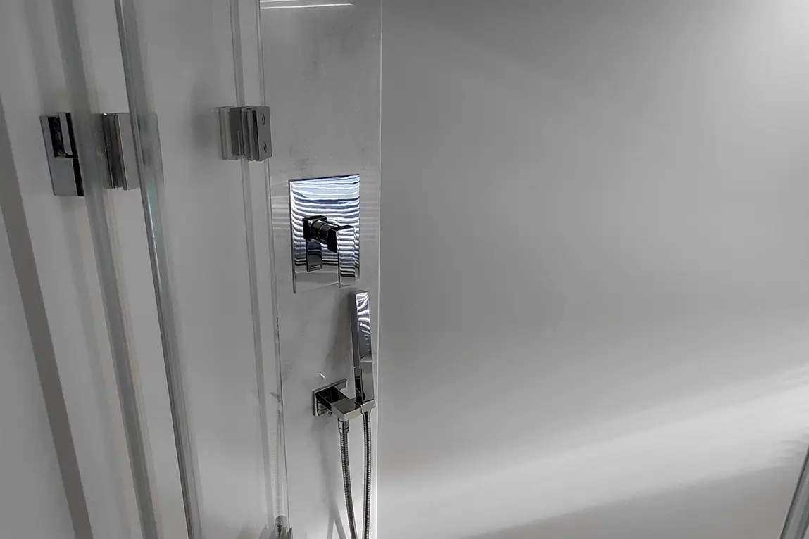 Chrome shower control and handset visible beside sliding glass shower door, against a light marble background.